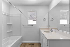 Bathroom featuring bathtub / shower combination, wood finished floors, visible vents, vanity, and baseboards