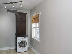 Clothes washing area featuring washer / dryer, a textured ceiling, light tile patterned floors, and cabinets