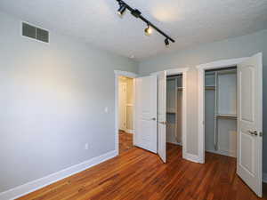 Unfurnished bedroom with a textured ceiling, a closet, track lighting, and dark hardwood / wood-style floors