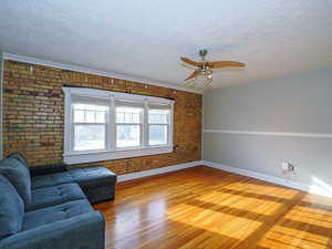 Unfurnished living room with ceiling fan, hardwood / wood-style floors, a textured ceiling, and brick wall