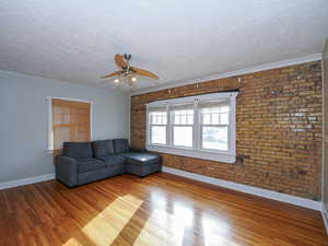 Unfurnished living room featuring brick wall, hardwood / wood-style floors, a textured ceiling, and ceiling fan