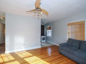 Living room featuring washer / dryer, a textured ceiling, ceiling fan, and hardwood / wood-style floors