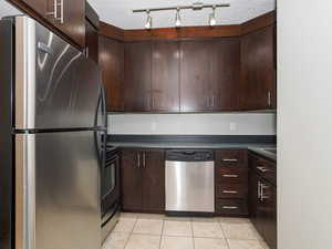 Kitchen with a textured ceiling, light tile patterned floors, dark brown cabinets, and appliances with stainless steel finishes