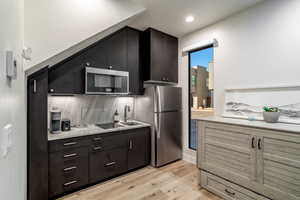 Kitchen with sink, decorative backsplash, light hardwood / wood-style flooring, and appliances with stainless steel finishes