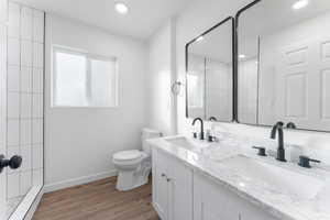 Bathroom with toilet, a tile shower, vanity, and hardwood / wood-style flooring