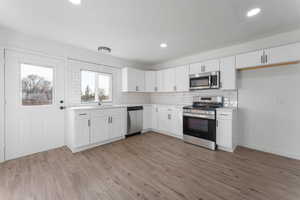 Kitchen with white cabinetry, appliances with stainless steel finishes, decorative backsplash, sink, and light hardwood / wood-style flooring