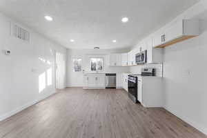 Kitchen with white cabinets, a textured ceiling, light wood-type flooring, tasteful backsplash, and appliances with stainless steel finishes