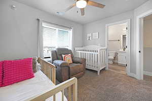 Carpeted bedroom featuring a crib, ensuite bathroom, and ceiling fan