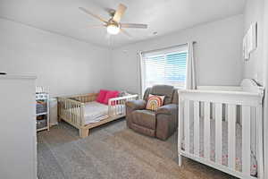 Carpeted bedroom with a crib and ceiling fan