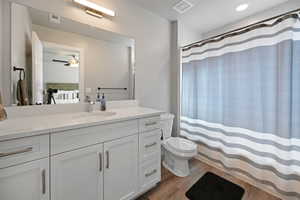 Bathroom with curtained shower, ceiling fan, wood-type flooring, toilet, and vanity