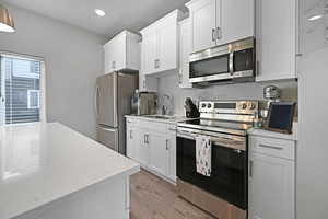 Kitchen with white cabinets, sink, light hardwood / wood-style flooring, light stone countertops, and appliances with stainless steel finishes