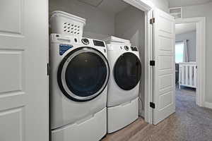 Clothes washing area with washing machine and clothes dryer and light colored carpet