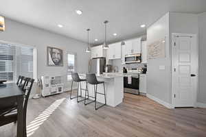 Kitchen featuring white cabinetry, a kitchen island, decorative light fixtures, and appliances with stainless steel finishes