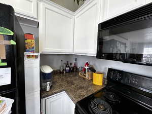 Kitchen featuring black appliances, white cabinetry, and dark stone counters