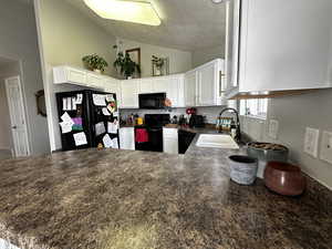 Kitchen with sink, kitchen peninsula, lofted ceiling, white cabinets, and black appliances