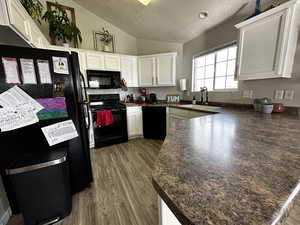 Kitchen with a textured ceiling, vaulted ceiling, sink, black appliances, and white cabinetry