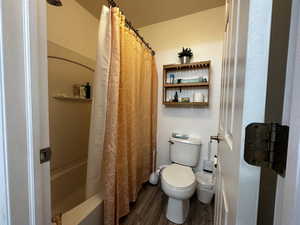 Bathroom featuring wood-type flooring, toilet, and shower / tub combo with curtain