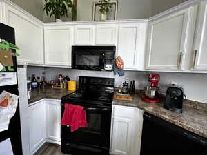 Kitchen with dark hardwood / wood-style flooring, white cabinetry, dark stone countertops, and black appliances