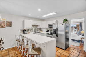 Kitchen featuring tile counters, stainless steel appliances, kitchen peninsula, sink, and white cabinetry