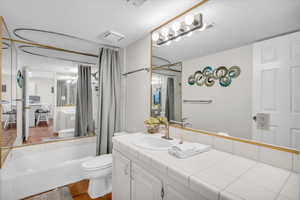 Full bathroom featuring toilet, a textured ceiling, shower / bath combination with curtain, and vanity