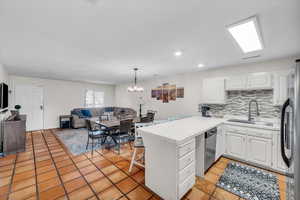 Kitchen with stainless steel appliances, sink, white cabinetry, tile countertops, and kitchen peninsula