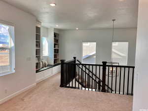 Hall with carpet, a textured ceiling, an inviting chandelier, and built in shelves