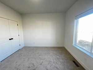 Unfurnished bedroom with light colored carpet, a closet, and multiple windows