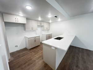 Kitchen with white cabinetry, dark wood-type flooring, kitchen peninsula, and a textured ceiling