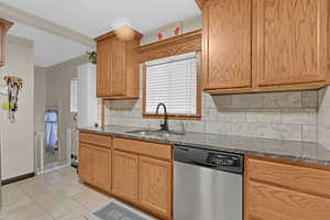 Kitchen with backsplash, dark stone counters, sink, stainless steel dishwasher, and light tile patterned floors