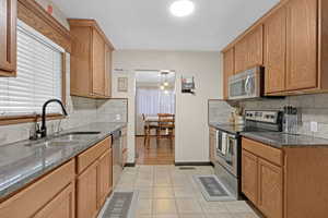 Kitchen with an inviting chandelier, sink, decorative backsplash, light tile patterned floors, and appliances with stainless steel finishes