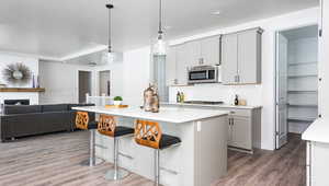 Kitchen with a kitchen bar, gray cabinetry, stainless steel appliances, a kitchen island with sink, and decorative backsplash