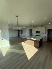 Kitchen featuring hardwood / wood-style floors, a center island with sink, a notable chandelier, sink, and white cabinetry