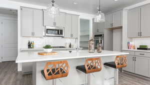 Kitchen featuring appliances with stainless steel finishes, a kitchen island with sink, a breakfast bar area, and gray cabinetry