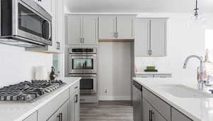 Kitchen featuring sink, hardwood / wood-style flooring, gray cabinets, appliances with stainless steel finishes, and light stone counters