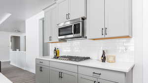 Kitchen with light stone countertops, appliances with stainless steel finishes, dark wood-type flooring, and backsplash