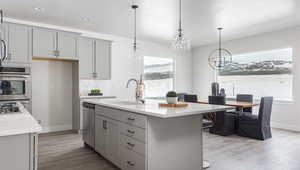 Kitchen with sink, gray cabinetry, wood-type flooring, an island with sink, and decorative light fixtures