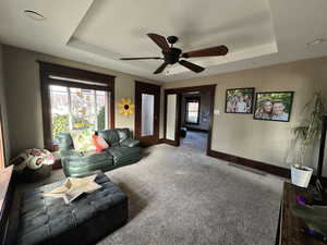 Carpeted living room featuring ceiling fan and a tray ceiling