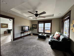 Carpeted living room with ceiling fan and a tray ceiling