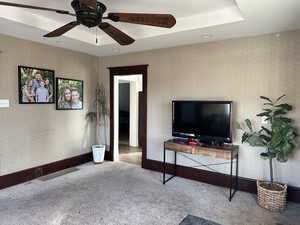 Living room with ceiling fan, light colored carpet, and a raised ceiling