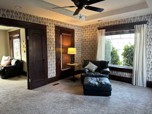 Living area featuring carpet floors, ceiling fan, and a raised ceiling