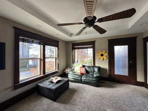 Carpeted living room with ceiling fan and a tray ceiling