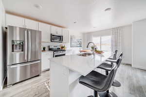 Kitchen featuring white cabinets, stainless steel appliances, an island with sink, a breakfast bar, and sink