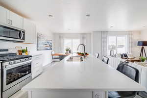 Kitchen with appliances with stainless steel finishes, an island with sink, a breakfast bar, sink, and white cabinetry