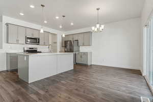 Kitchen featuring hanging light fixtures, appliances with stainless steel finishes, a kitchen island with sink, and gray cabinetry