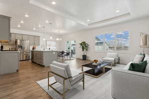 Living room with an inviting chandelier, a raised ceiling, sink, a textured ceiling, and light hardwood / wood-style floors