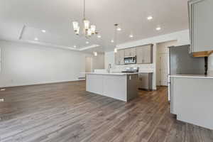 Kitchen with appliances with stainless steel finishes, a raised ceiling, a kitchen island with sink, gray cabinets, and hanging light fixtures