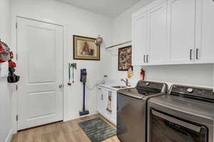 Laundry room with washer and dryer, cabinets, light hardwood / wood-style floors, and sink