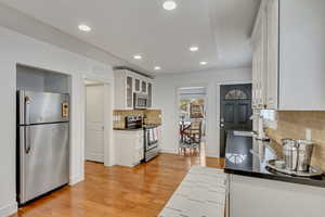 Kitchen with tasteful backsplash, appliances with stainless steel finishes, white cabinets, light hardwood / wood-style flooring, and sink