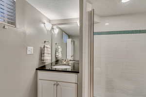 Bathroom featuring a shower with door, vanity, and a textured ceiling