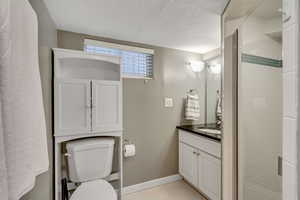 Bathroom with toilet, a textured ceiling, walk in shower, tile patterned floors, and vanity